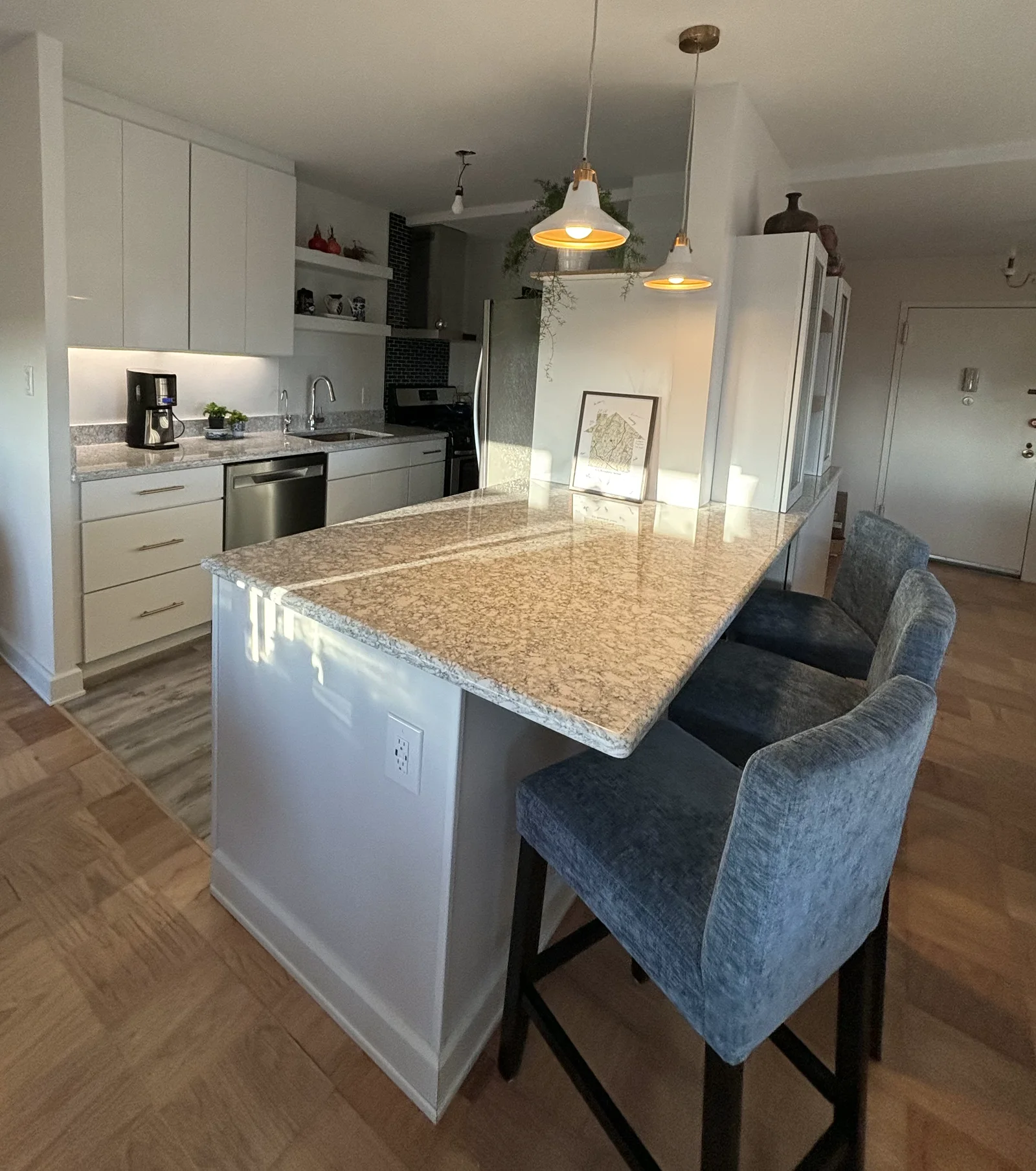 Renovated Glen Ridge galley kitchen with white cabinets, a speckled seating counter, upholstered stools, and pendant lights