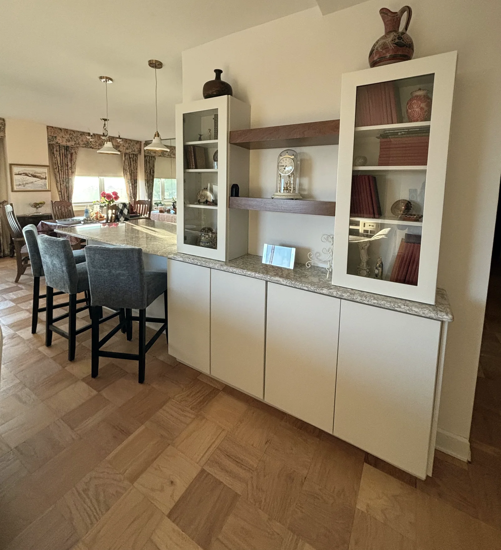 White storage and glass-front display cabinets with wood shelves beside the kitchen seating area