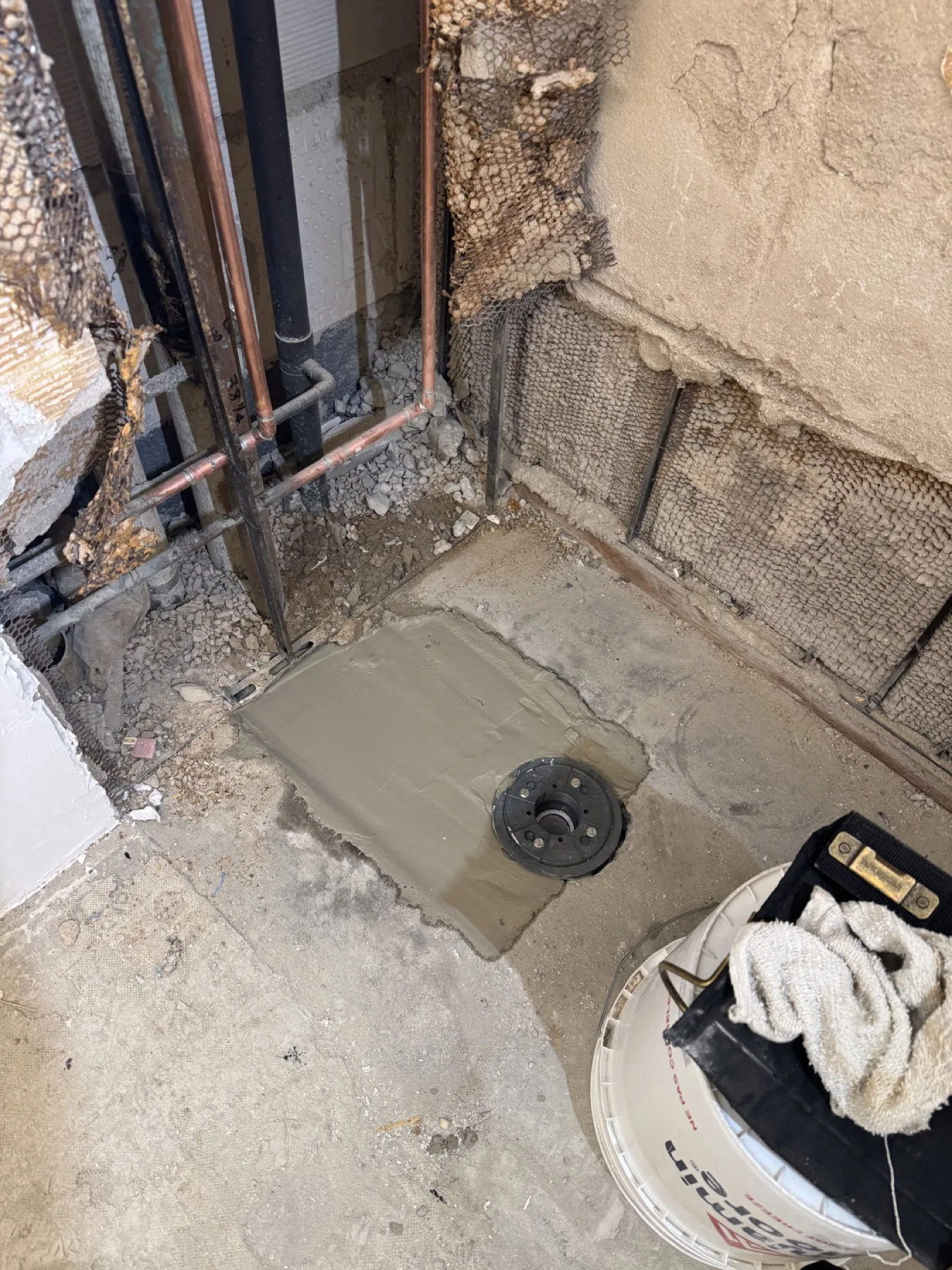 Exposed wall lath and plumbing with floor preparation around the toilet flange during the bathroom renovation